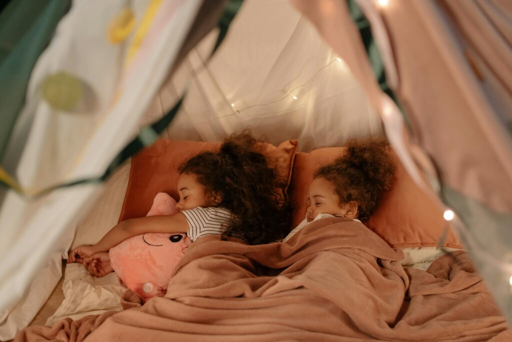Two young sisters sleeping in a cozy blanket fort, creating warm childhood memories.